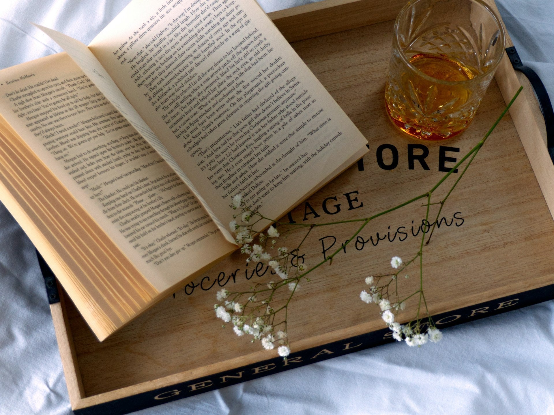 A tray with a flower stem, an open book and a glass of neat whisky.