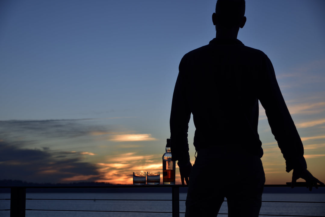 A man enjoying a sunset with a glass of whisky.