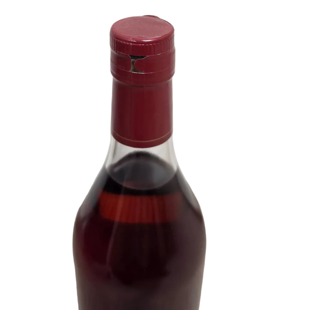 A close-up of a dark glass bottle with a deep red wax seal and a cream-colored label, set against a white paneled wall and carpeted floor.