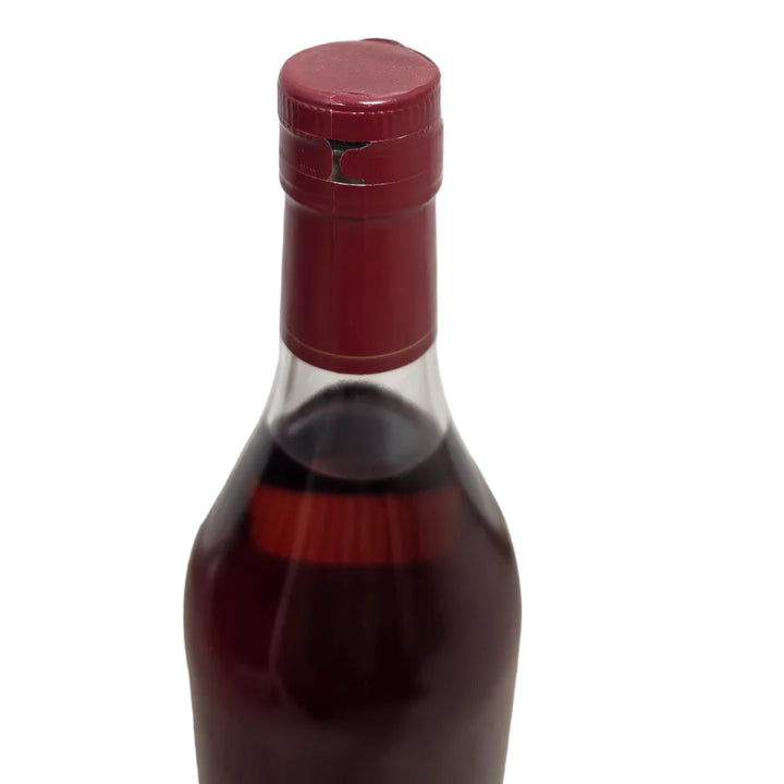 A close-up of a dark glass bottle with a deep red wax seal and a cream-colored label, set against a white paneled wall and carpeted floor.