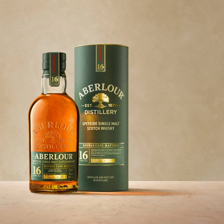A bottle of Aberlour 16 Year Old Double Cask Single Malt Scotch Whisky stands beside its matching cylindrical box on a neutral background, both with gold and white labels accented with green, emphasizing its double cask maturation.