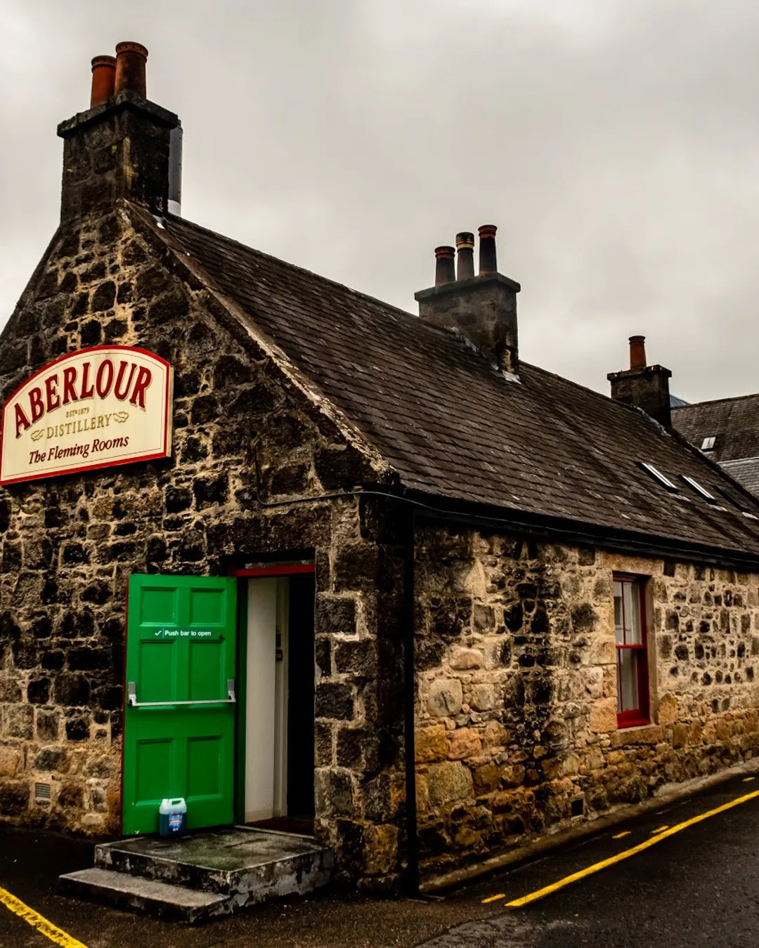 Stone building with a green door and Aberlour sign on a cloudy day