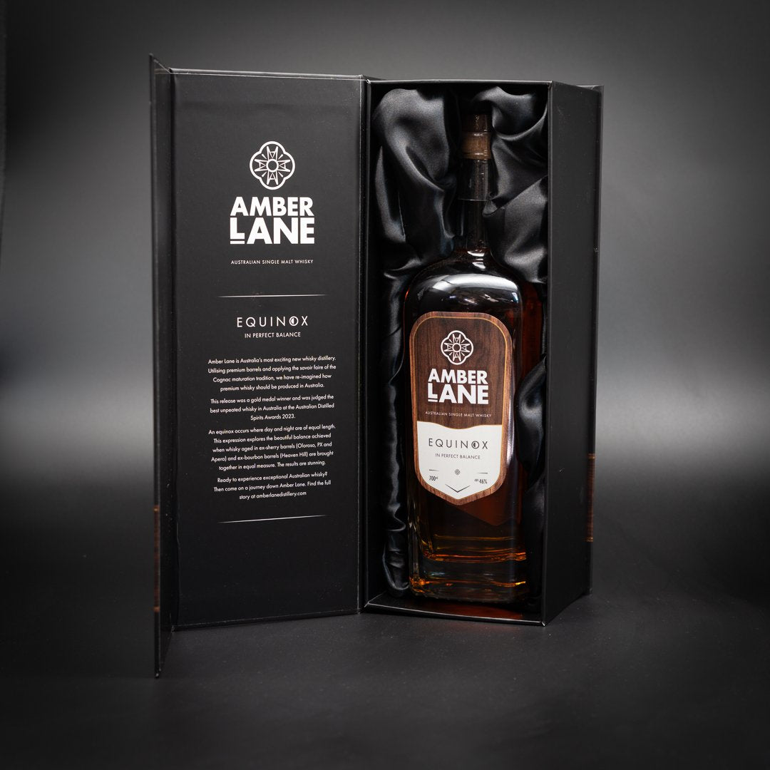 A bottle of Amber Lane Equinox Australian Single Malt Whisky sits in an open black silk-lined box, its label and product details visible on the inside cover, all set against a dark background.