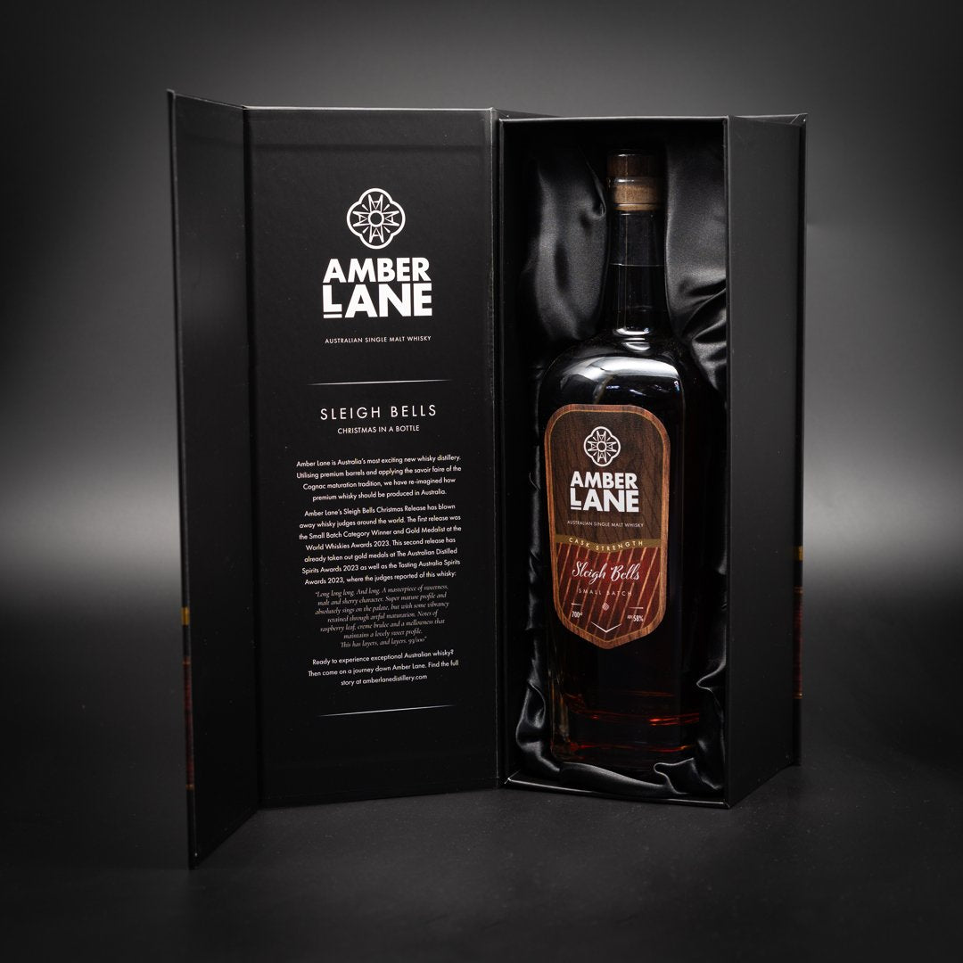 A 700ml bottle of Amber Lane Sleigh Bells Australian Single Malt Whisky is showcased in an elegant black gift box with gold accents, beside a panel detailing the brand and its sherry-cask whisky.