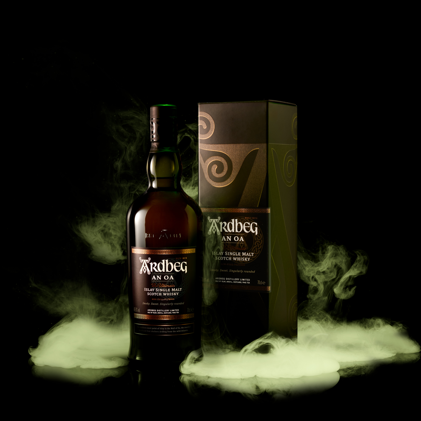 A bottle of Ardbeg An Oa Single Malt Scotch Whisky stands next to its box, both wrapped in greenish smoke against a black background—a striking display for this renowned peated Scotch.