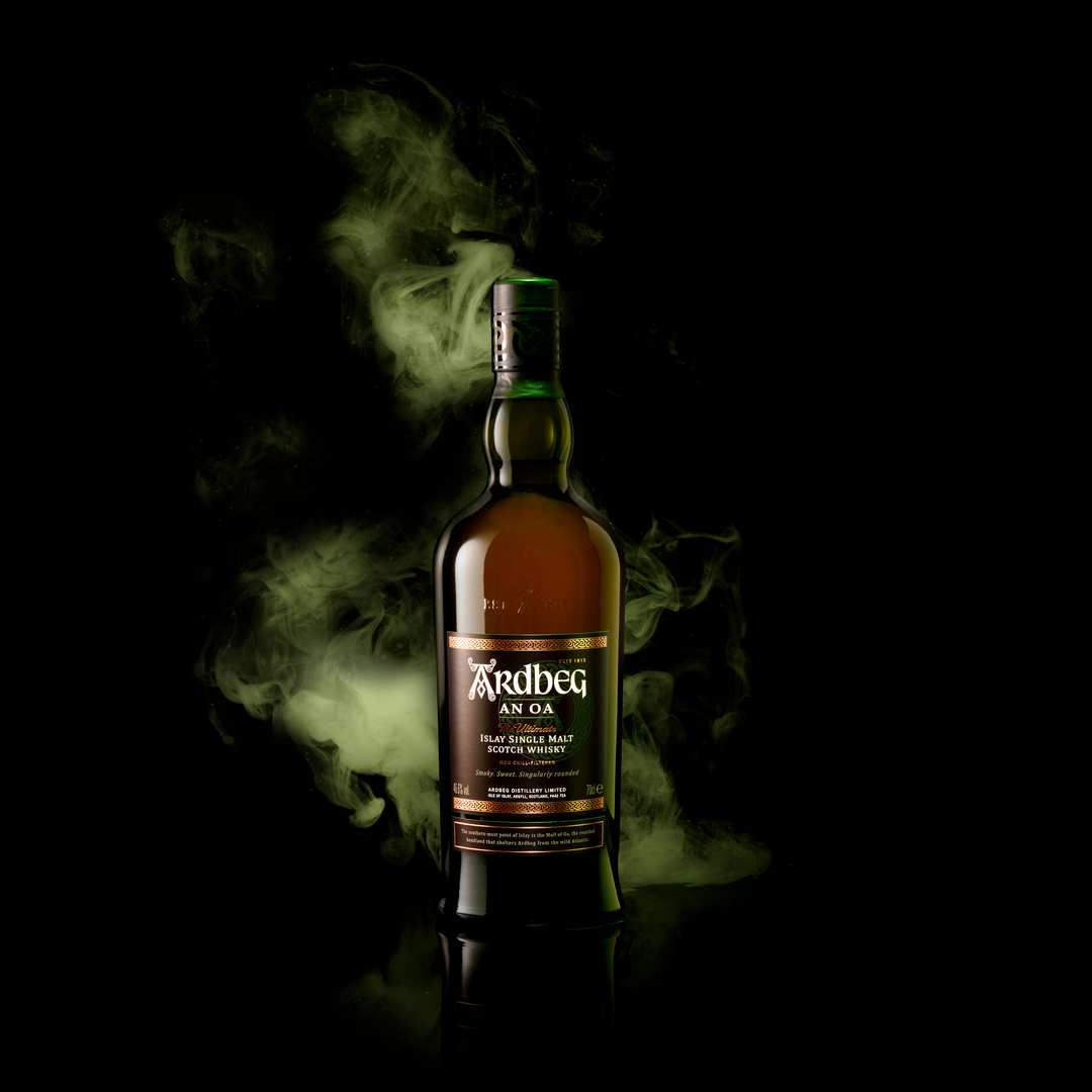 A bottle of Ardbeg An Oa Single Malt Scotch Whisky stands upright on a black background, enveloped in swirling green smoke.