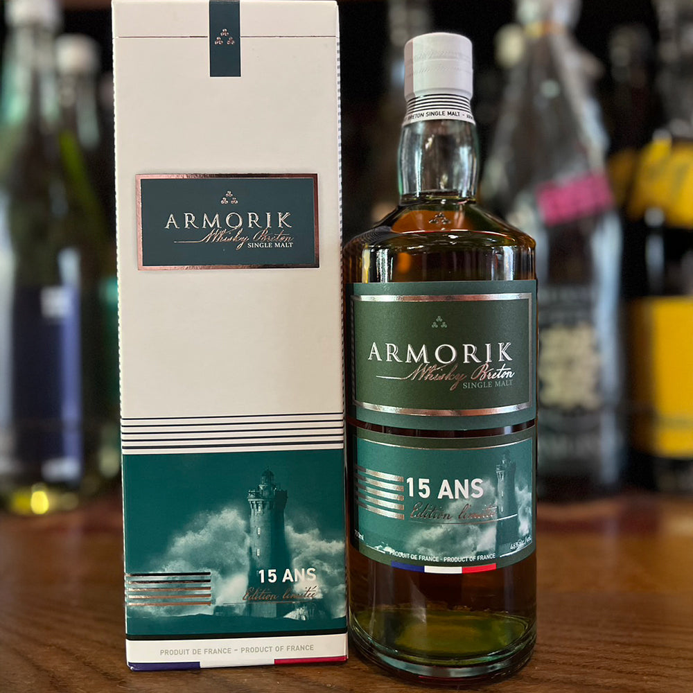 A bottle of Armorik 15 Ans (15 Year Old) French Single Malt Whisky is displayed beside its box on a wooden surface, set against a blurred bar background, reflecting its refined character.