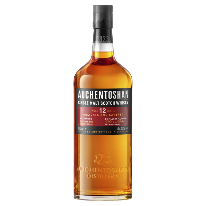 A bottle of Auchentoshan 12 Year Old Single Malt Scotch Whisky features a black cap, amber liquid, and a red and white label displaying triple distilled details, age, flavor notes, and distillery information.