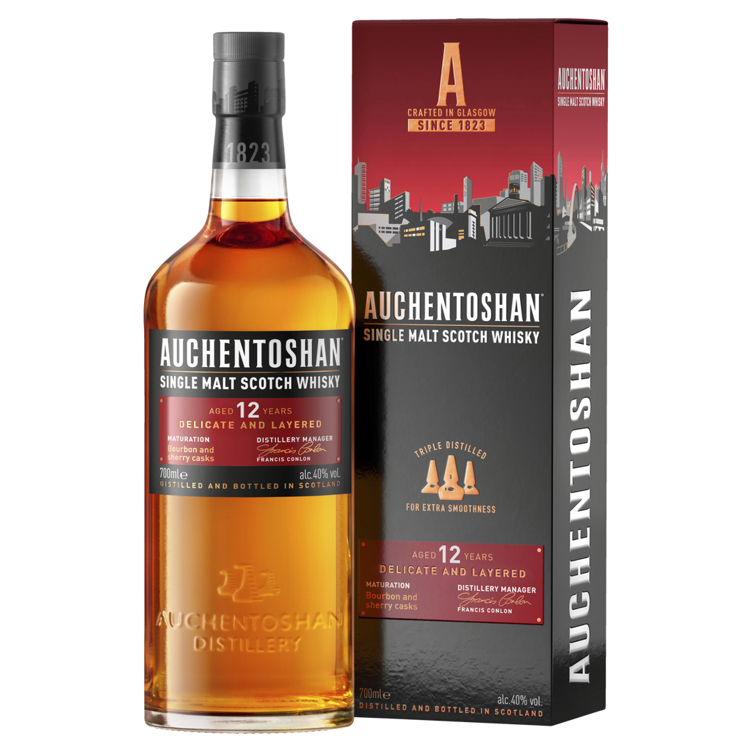 Auchentoshan 12 Year Old Single Malt Scotch Whisky stands beside its branded box, both with orange and white accents that emphasize its Scottish heritage and signature triple distillation.