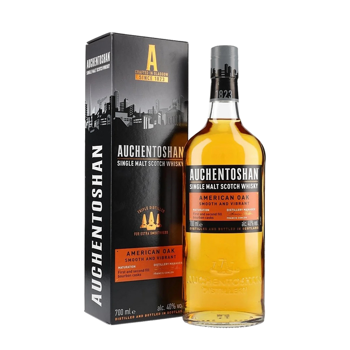 A bottle of Auchentoshan American Oak Single Malt Scotch Whisky is shown next to its black and orange box with a city skyline graphic and "Smooth and Vibrant" text.