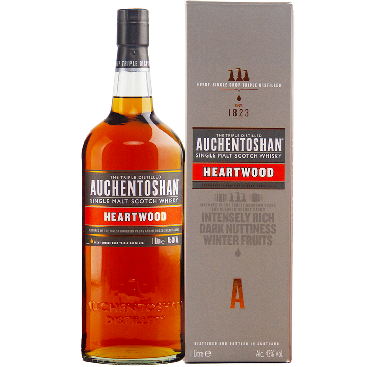A 1L bottle of Auchentoshan Heartwood Single Malt Scotch Whisky, a travel retail exclusive, stands beside its grey box, both featuring the brand and product details in red, white, and gold.
