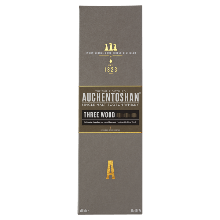 A box of Auchentoshan Three Wood Single Malt Scotch Whisky features gold and white text on a gray background, prominently displaying the brand logo, whisky details, and highlighting its triple maturation process.