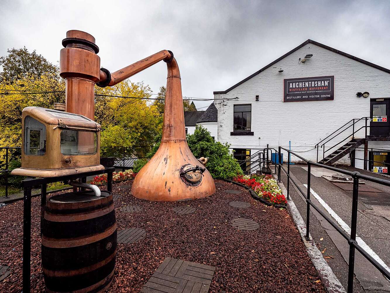 Large wooden whiskey still sculpture in front of a building with 'Archentferns' sign.
