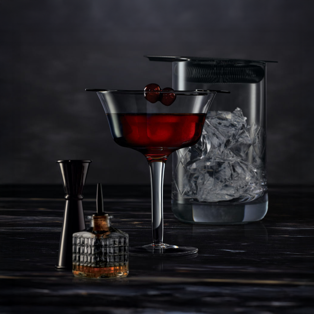 A dark cocktail made with Baker’s 7 Year Old Single Barrel Bourbon is garnished with two cherries in a glass, set beside a jigger, a dropper bottle, and an ice-filled mixing glass topped with a strainer on a marbled surface.