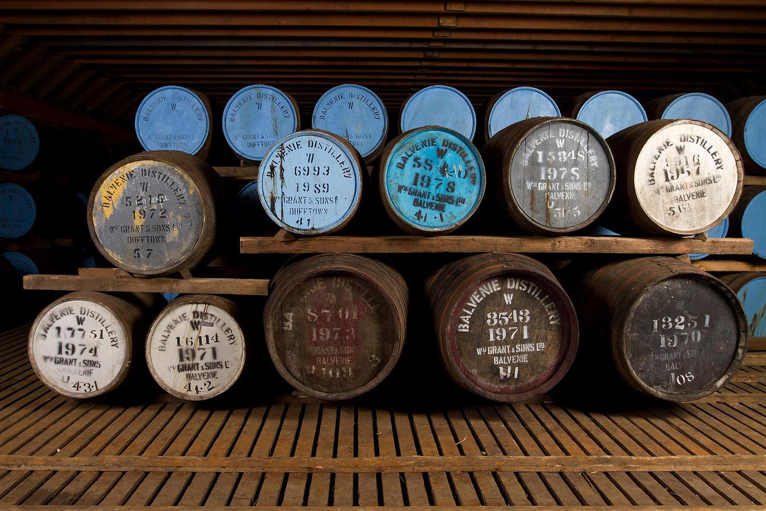 Stack of wine barrels with vintage labels in a wooden cellar.