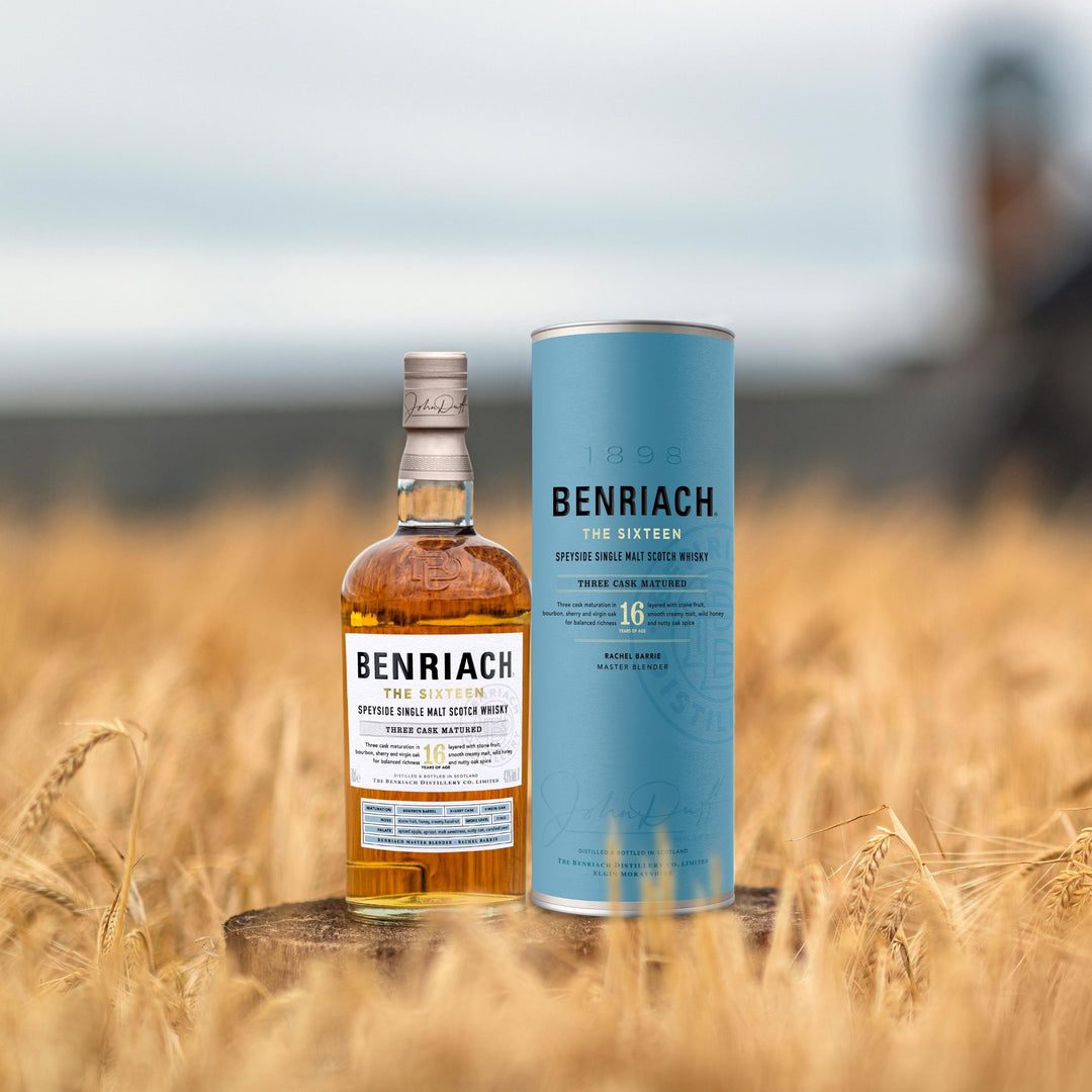 A bottle of Benriach The Sixteen Single Malt Scotch Whisky with its blue cylindrical packaging stands in a golden wheat field, emphasizing the smooth character of this triple cask matured release.