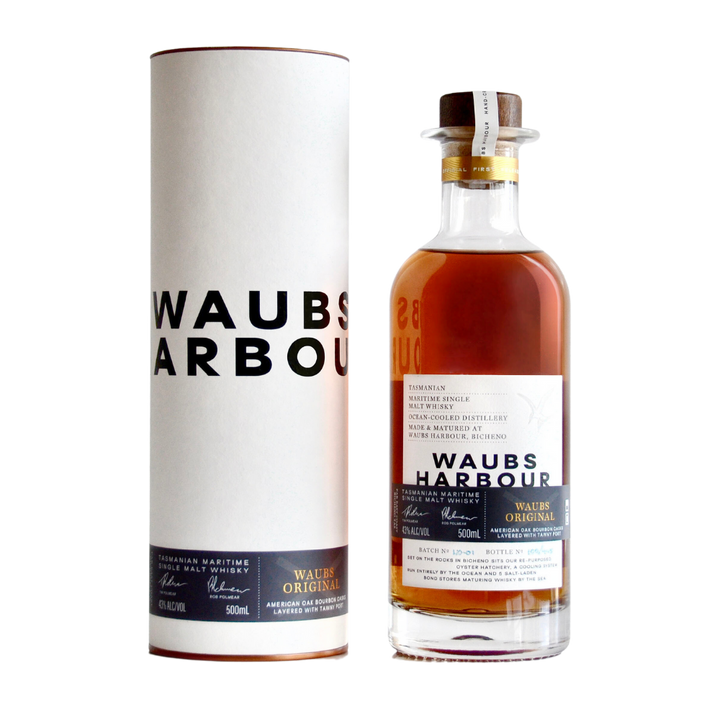 A bottle of Waubs Harbour Original Tasmanian Single Malt Whisky with a corked cap stands beside its cylindrical white packaging, both featuring the brand’s bold black logo. The bottle contains premium amber whisky.