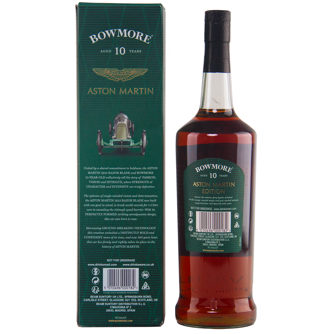 A bottle of Bowmore 10 Year Old Aston Martin Edition 7 Single Malt Scotch Whisky stands next to its green box, featuring gold text and a vintage Aston Martin race car illustration. The label echoes the box’s design.