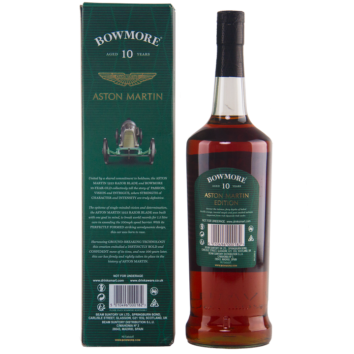A bottle of Bowmore 10 Year Old Aston Martin Edition 7 Single Malt Scotch Whisky stands next to its green box, featuring gold text and a vintage Aston Martin race car illustration. The label echoes the box’s design.