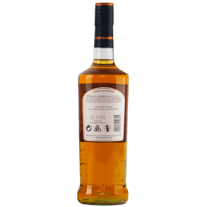 A bottle of Bowmore Legend Islay Single Malt Scotch Whisky is shown from the back on a plain white background, revealing amber peated whisky inside the clear glass and a white label with text and symbols.