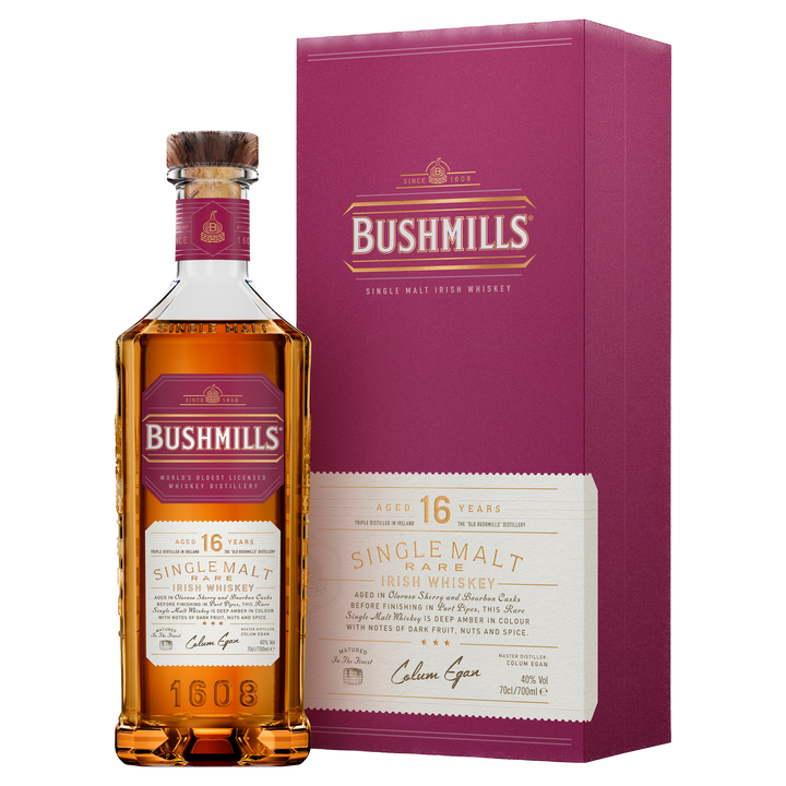 A bottle of Bushmills 16 Year Old Single Malt Irish Whiskey with a cork top stands beside its matching maroon box, both displaying gold and cream label details and product information.