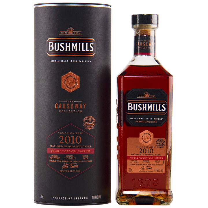 A bottle of Bushmills 2010 Double Moscatel Cask Single Malt whisky from the Causeway Collection stands beside its matching black and copper cylindrical box, both highlighting its unique cask maturation and Irish origin.