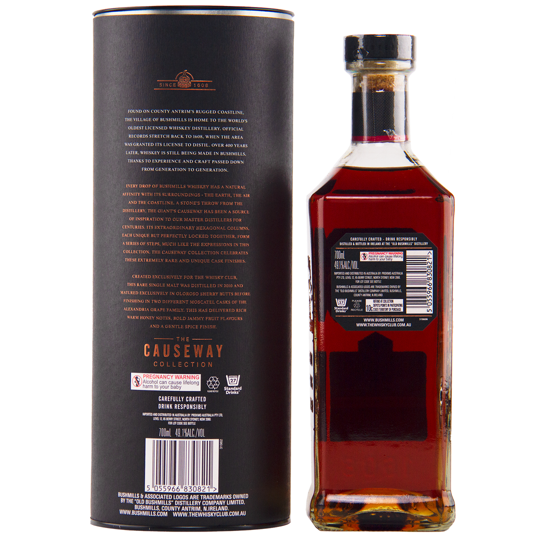 A bottle of Bushmills 2010 Double Moscatel Cask Single Malt whisky stands beside its cylindrical black packaging, both displaying gold and white text with product details and Causeway Collection branding. The bottle holds amber-hued whisky.