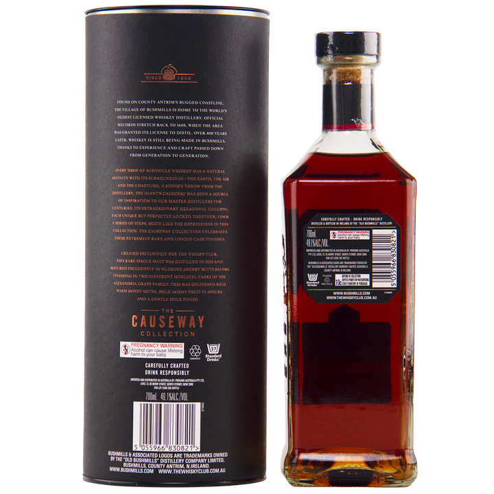 A bottle of Bushmills 2010 Double Moscatel Cask Single Malt whisky stands beside its cylindrical black packaging, both displaying gold and white text with product details and Causeway Collection branding. The bottle holds amber-hued whisky.