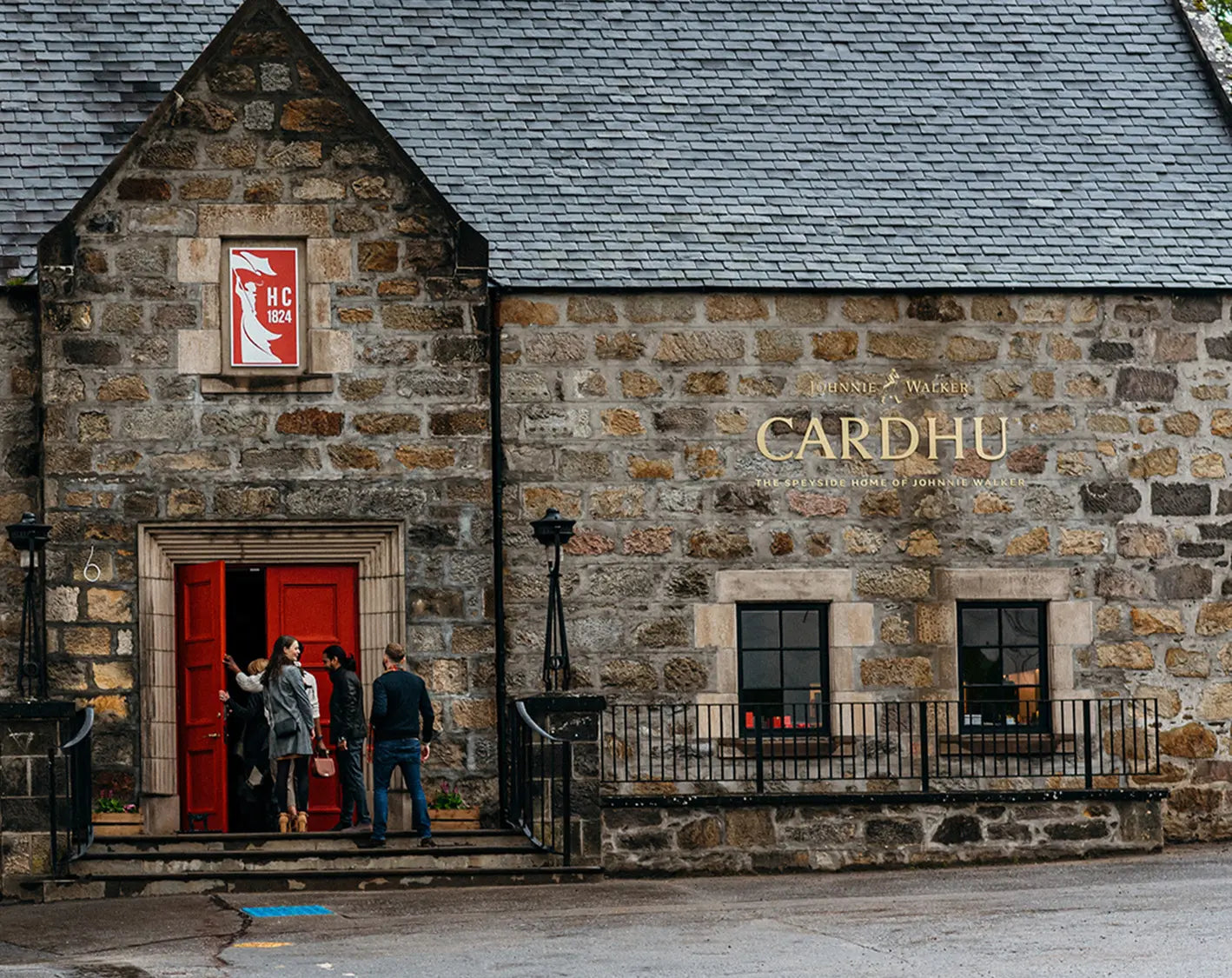 Stone building with 'Cardhu' branding and people standing outside a red door.