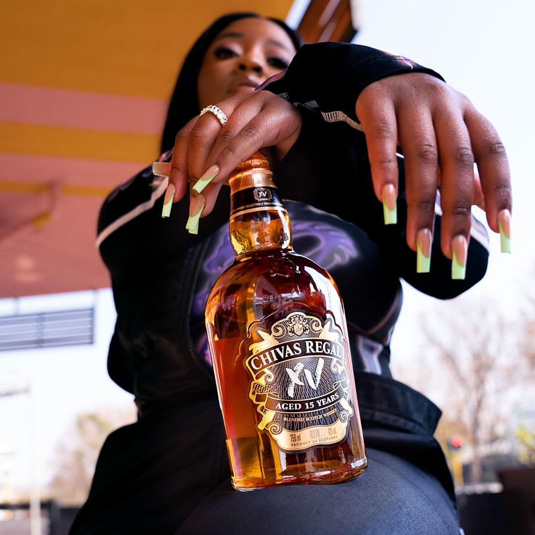 Person holding a bottle of Chivas Regal XV whiskey with a blurred background