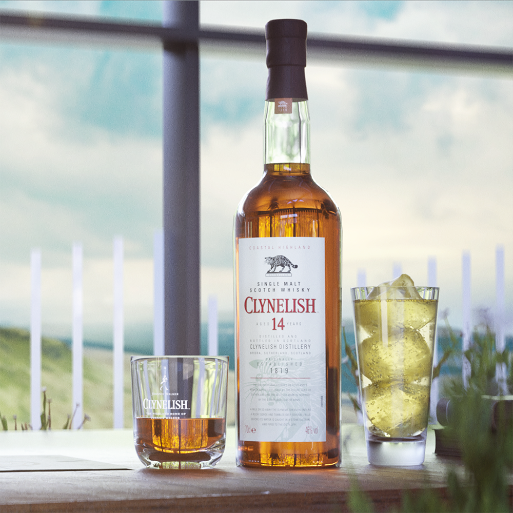 A bottle of Clynelish 14 Year Old Single Malt Whisky stands on a table between a whisky glass and an ice-filled glass, set against a scenic outdoor backdrop that reflects its coastal character.