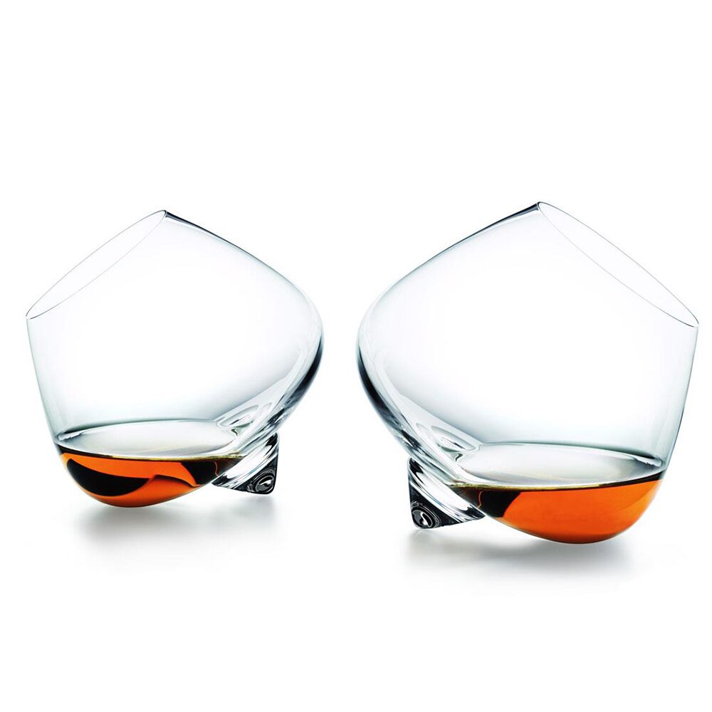 The Normann Copenhagen Cognac Glass 2 pcs features sleek, Scandinavian-inspired glassware with two tilted glasses—each holding amber liquid—arranged on their sides against a white background for a modern, artistic touch.