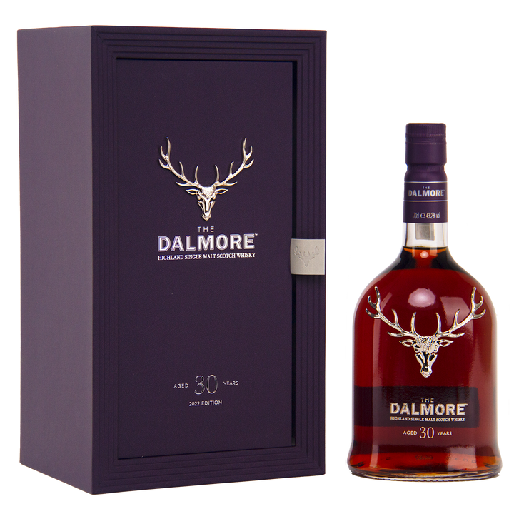 A bottle of The Dalmore 30 Year Old Single Malt Scotch Whisky stands next to its elegant dark purple box, both showcasing a silver stag logo and white text denoting the exclusive 2023 edition.
