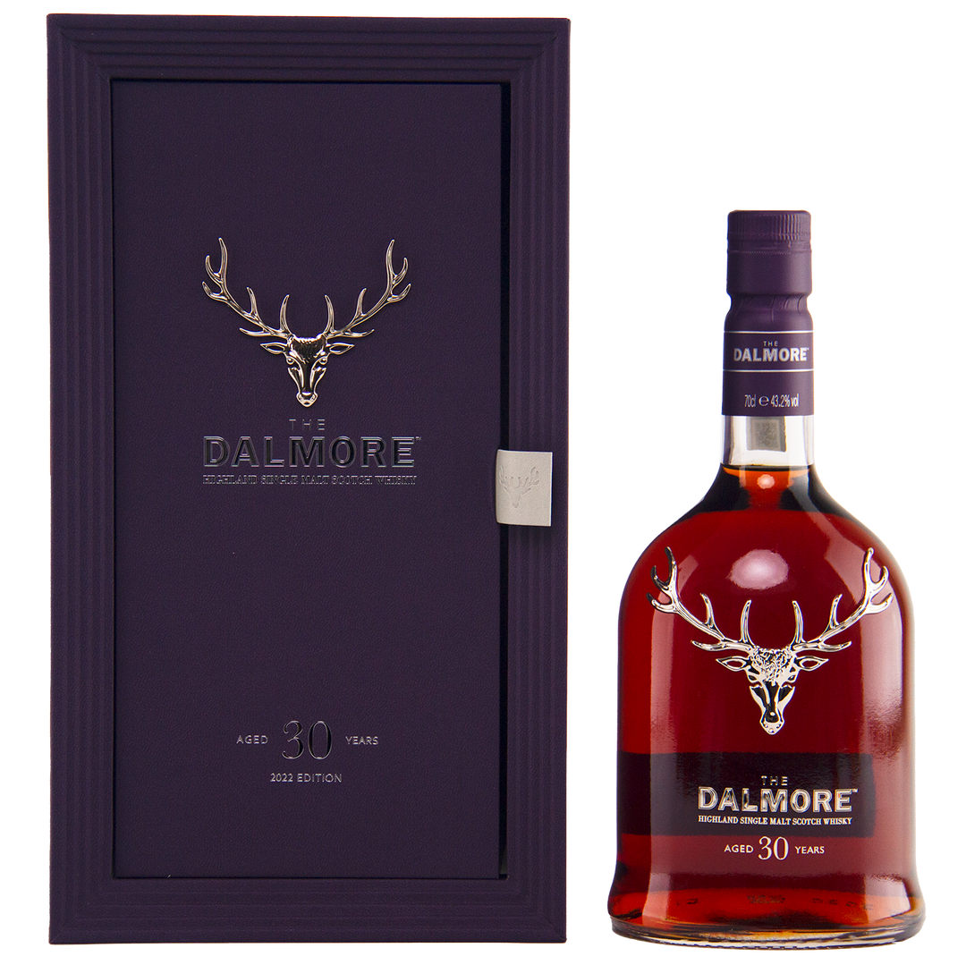A bottle of The Dalmore 30 Year Old Single Malt Scotch stands beside its elegant purple case, both adorned with a silver stag logo and refined labeling.