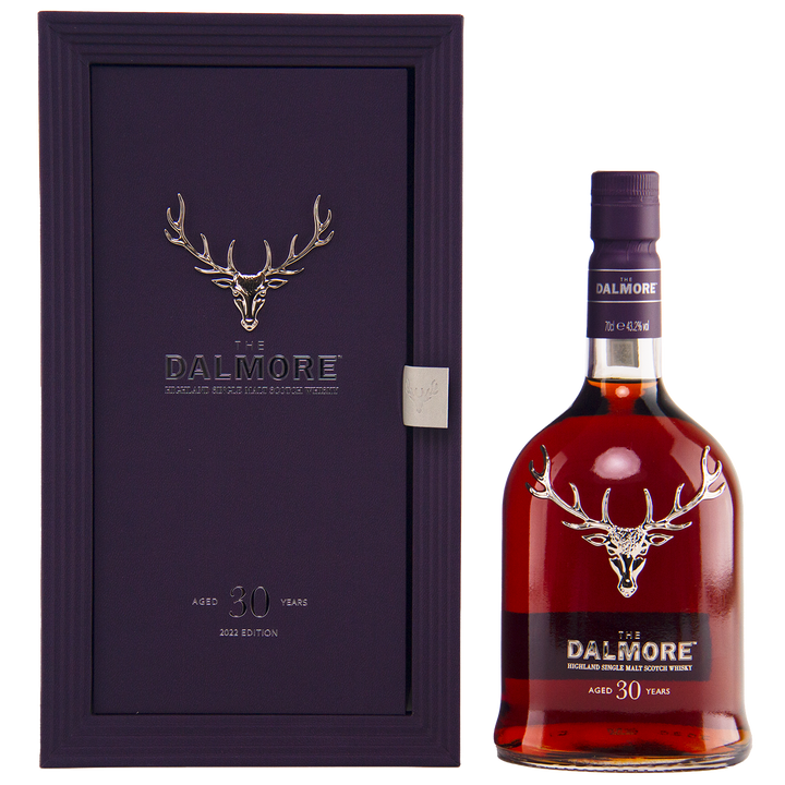 A bottle of The Dalmore 30 Year Old Single Malt Scotch stands beside its elegant purple case, both adorned with a silver stag logo and refined labeling.