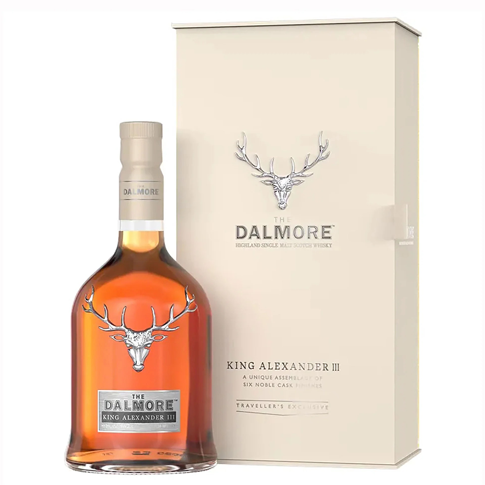 A bottle of The Dalmore King Alexander III Highland Single Malt Scotch Whisky is shown with its cream-colored box, both adorned with a silver stag head logo and elegant text. The amber bottle stands in front, highlighting this six-cask matured whisky.