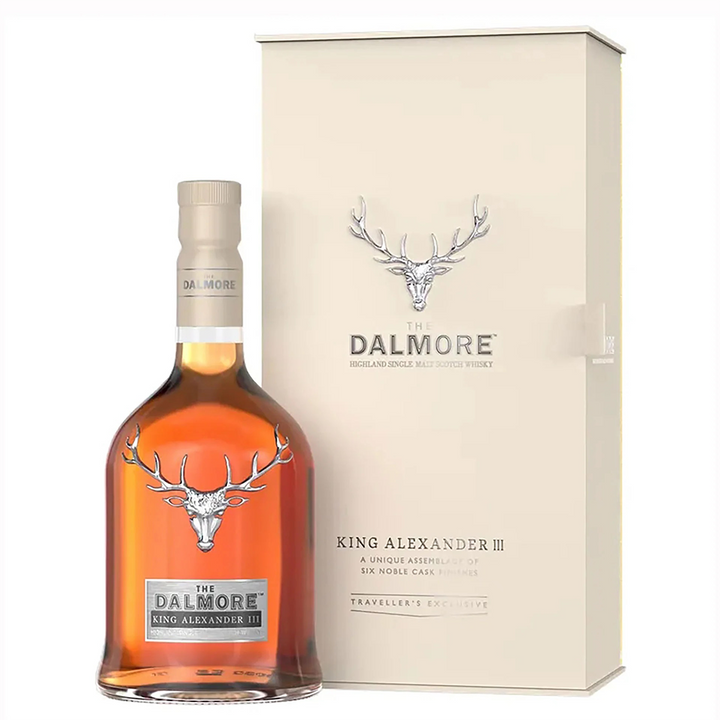 A bottle of The Dalmore King Alexander III Highland Single Malt Scotch Whisky is shown with its cream-colored box, both adorned with a silver stag head logo and elegant text. The amber bottle stands in front, highlighting this six-cask matured whisky.