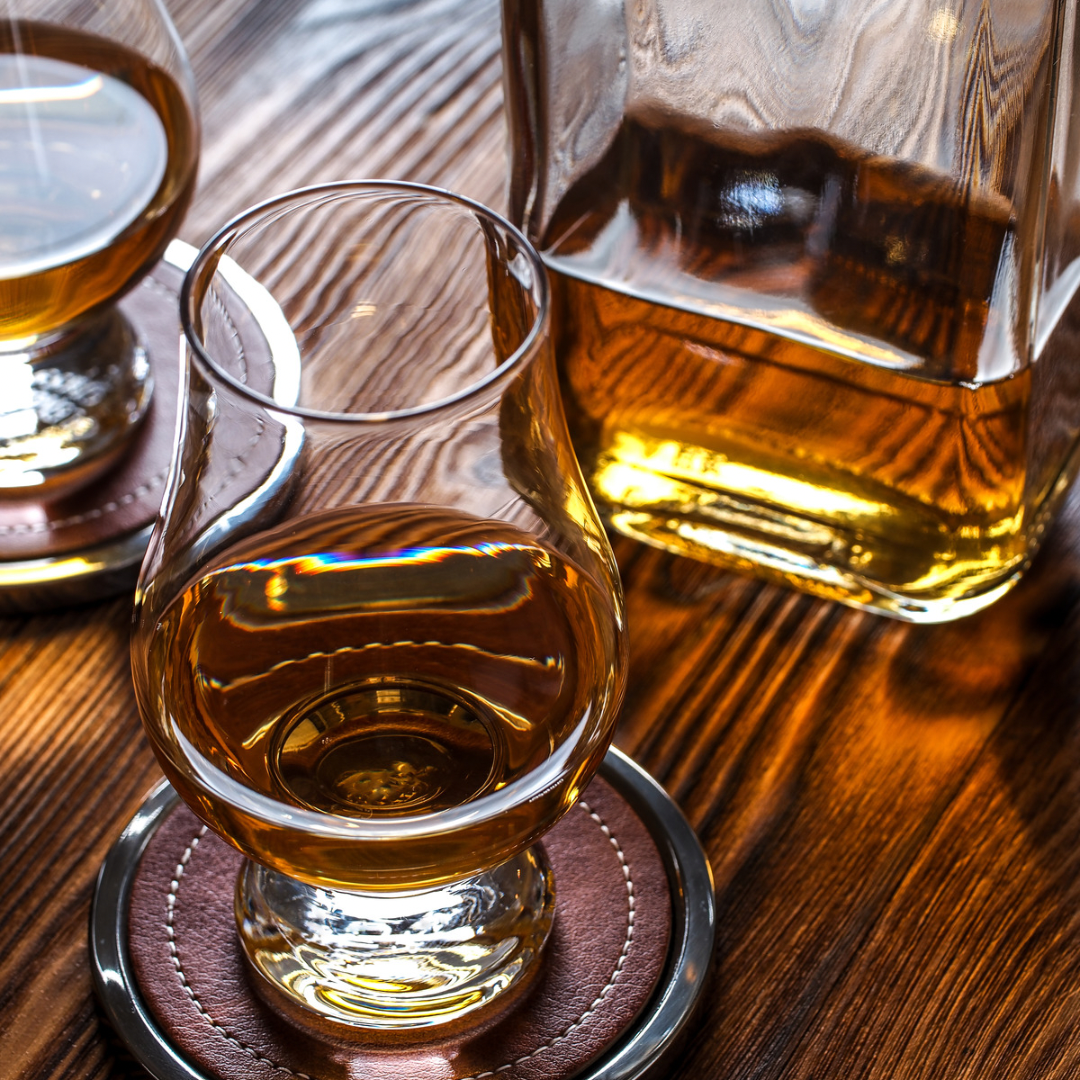 Glass of whiskey on a wooden coaster with a decanter in the background