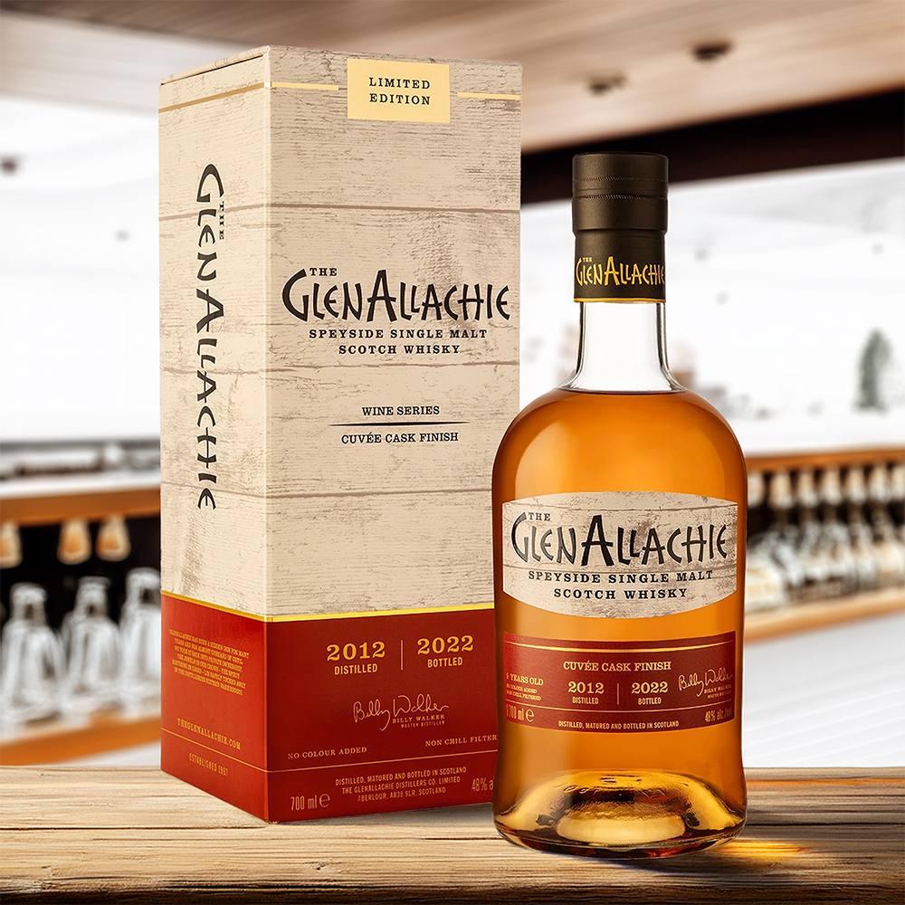 A bottle of GlenAllachie 9 Year Old Cuvée Wine Cask Single Malt Scotch Whisky stands beside its cream and gold box on a wooden surface, with blurred whisky bottles displayed on shelves in the background.