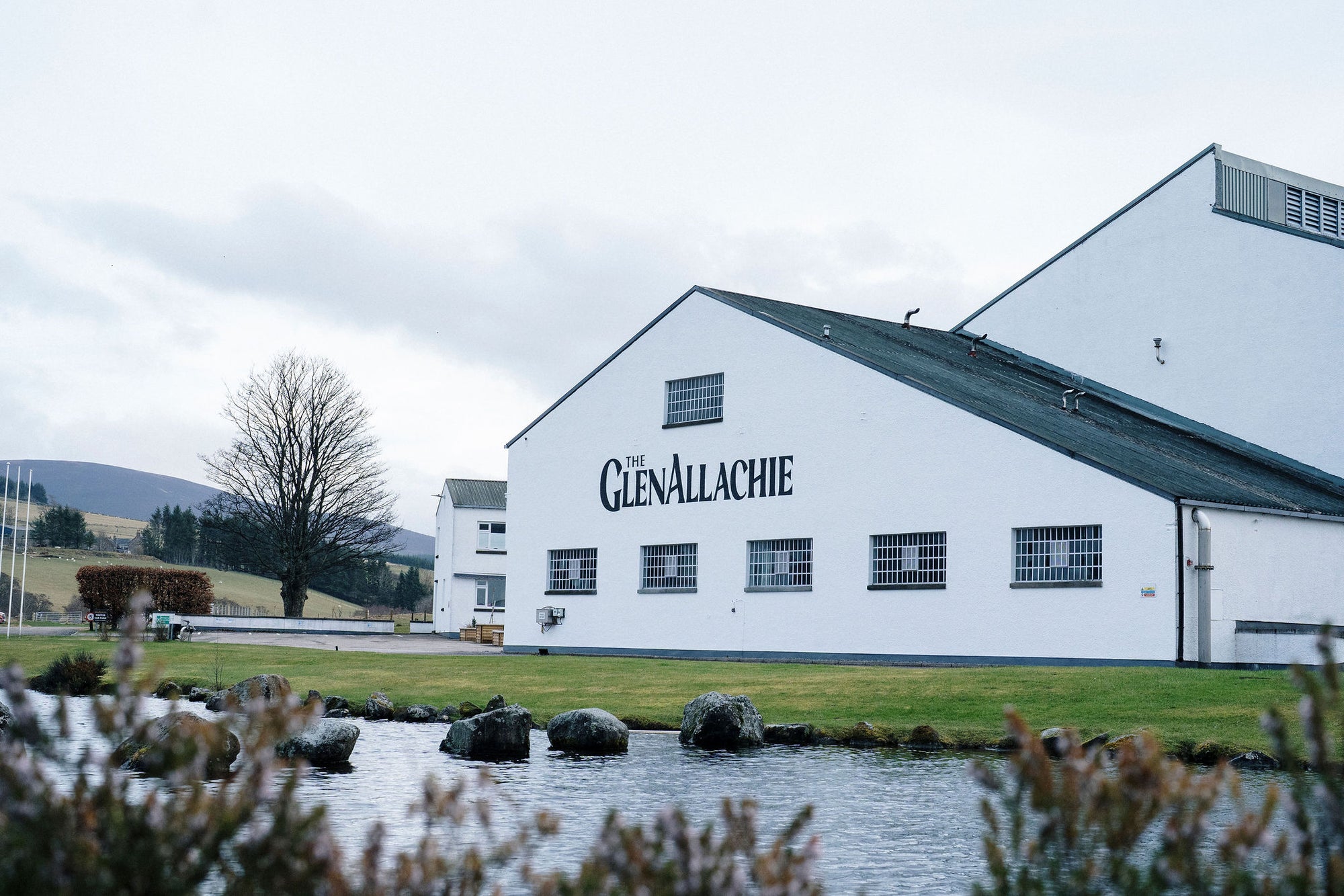 GlenAllachie distillery building with a lake and trees in the foreground