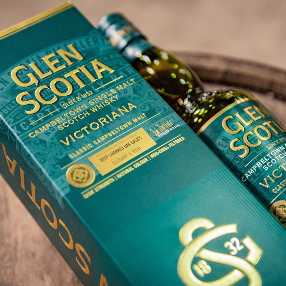 A bottle of Glen Scotia Victoriana Single Malt Scotch Whisky, partially in its teal and gold box, sits on a wooden surface. Finished in sherry casks, this elegant Campbeltown expression boasts character and depth.