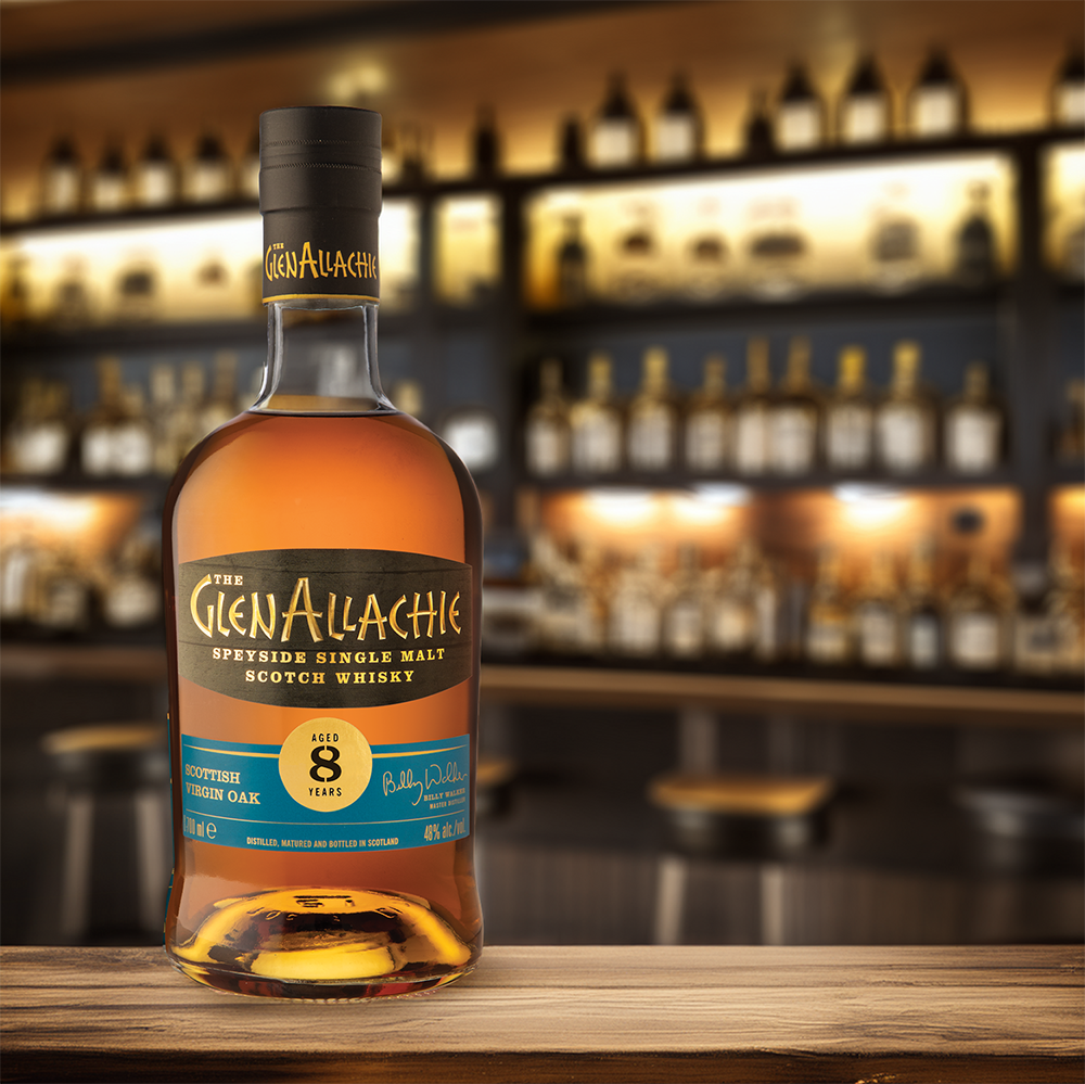 A bottle of GlenAllachie 8 Year Old Scottish Oak Single Malt Scotch Whisky stands on a wooden bar counter, with shelves of assorted liquor bottles softly blurred in the background.