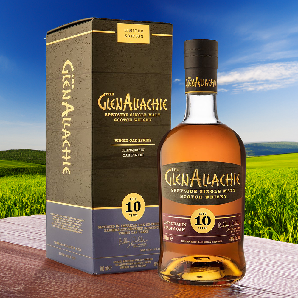 A bottle of GlenAllachie 10 Year Old Chinquapin Virgin Oak Finish Single Malt Scotch Whisky stands beside its box on a wooden surface, set against a lush green field and clear blue sky.