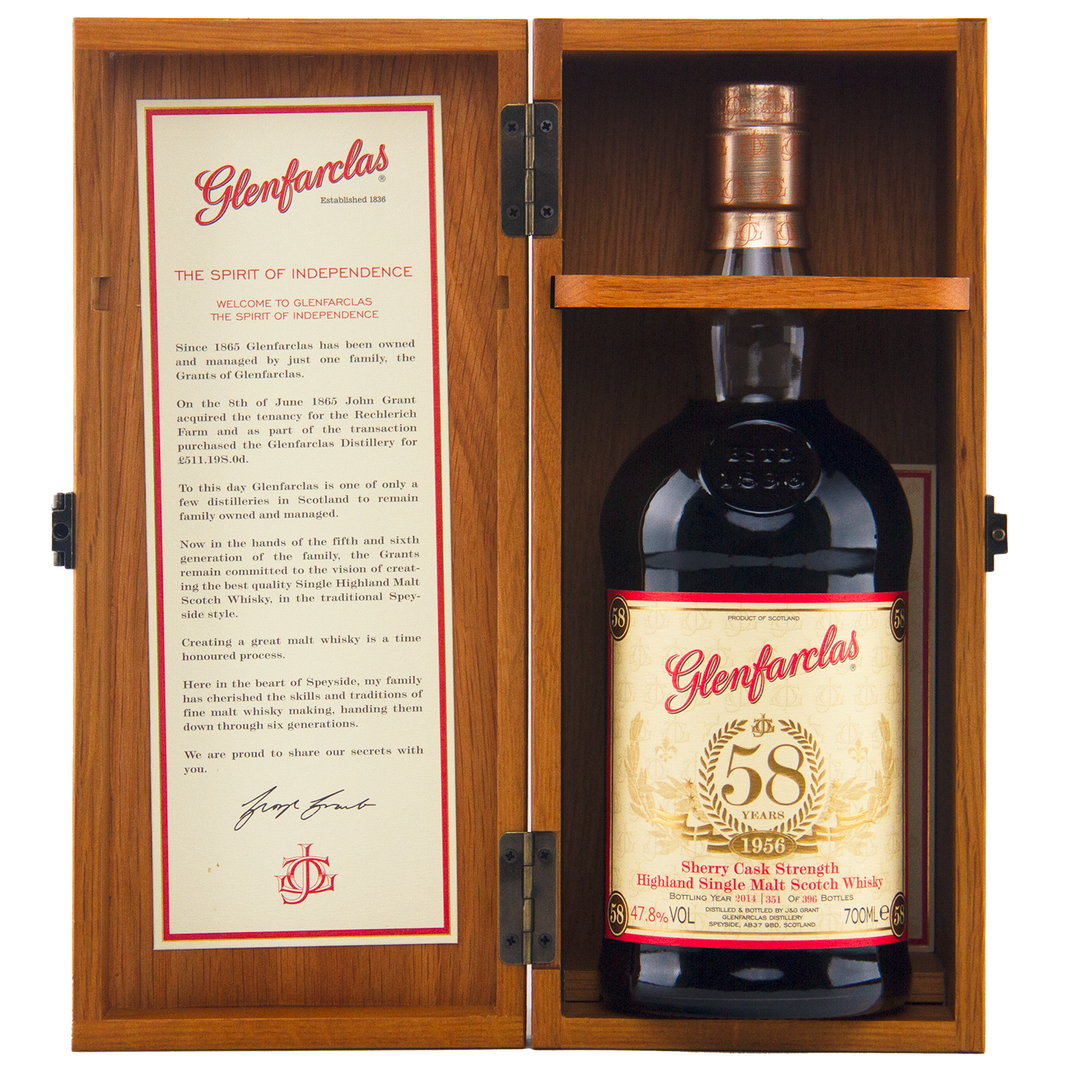 A bottle of Glenfarclas 1956 58 Year Old Sherry Cask Strength whisky is displayed in an open wooden box, with its description and history detailed on the inside of the left door.