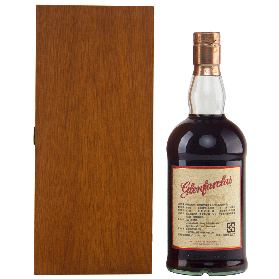 A bottle of Glenfarclas 1956 58 Year Old Sherry Cask Strength with a cream and red label stands next to a closed, tall wooden box against a white background.