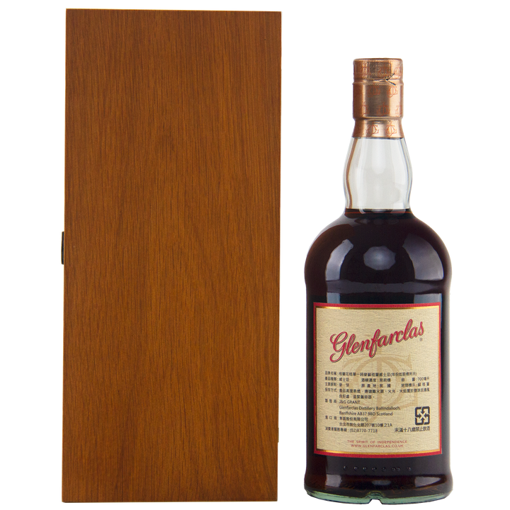 A bottle of Glenfarclas 1956 58 Year Old Sherry Cask Strength with a cream and red label stands next to a closed, tall wooden box against a white background.