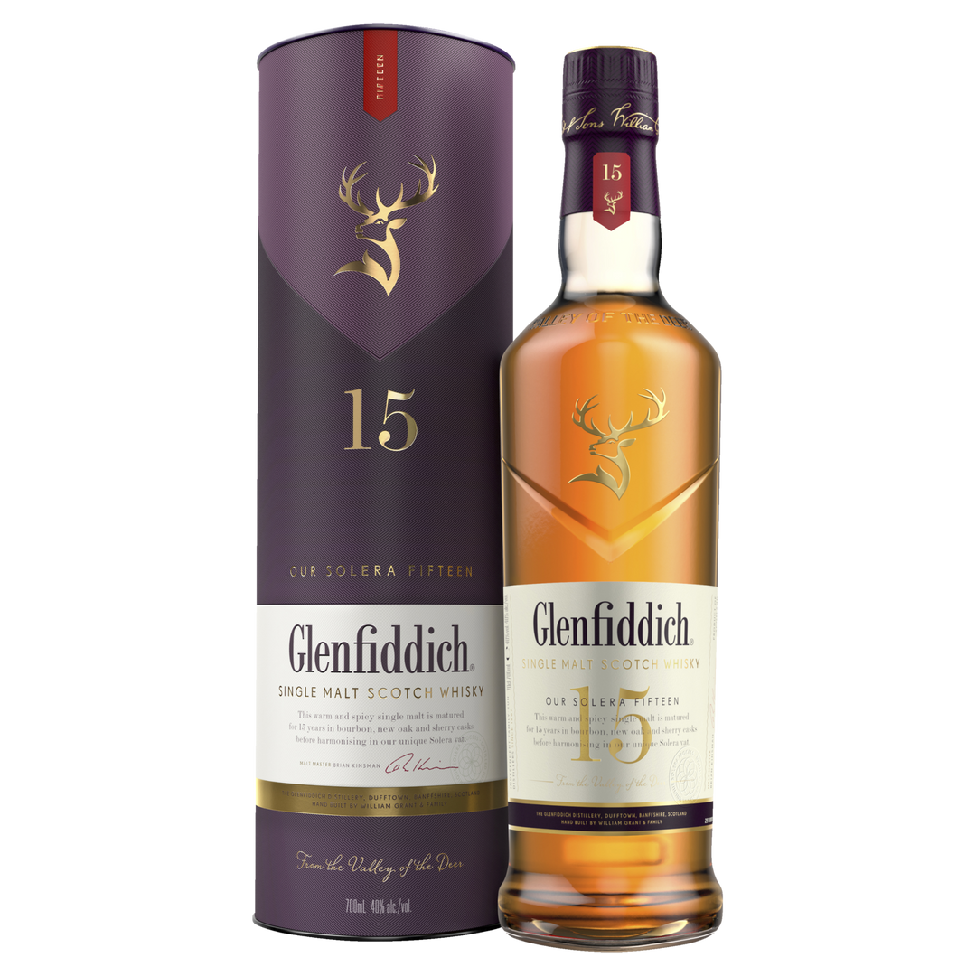 A Glenfiddich 15 Year Old Solera Reserve Single Malt Scotch Whisky bottle and its cylindrical packaging, both adorned with gold stag logos and purple-gold accents, display the “15” marking the whisky’s Solera Reserve identity.