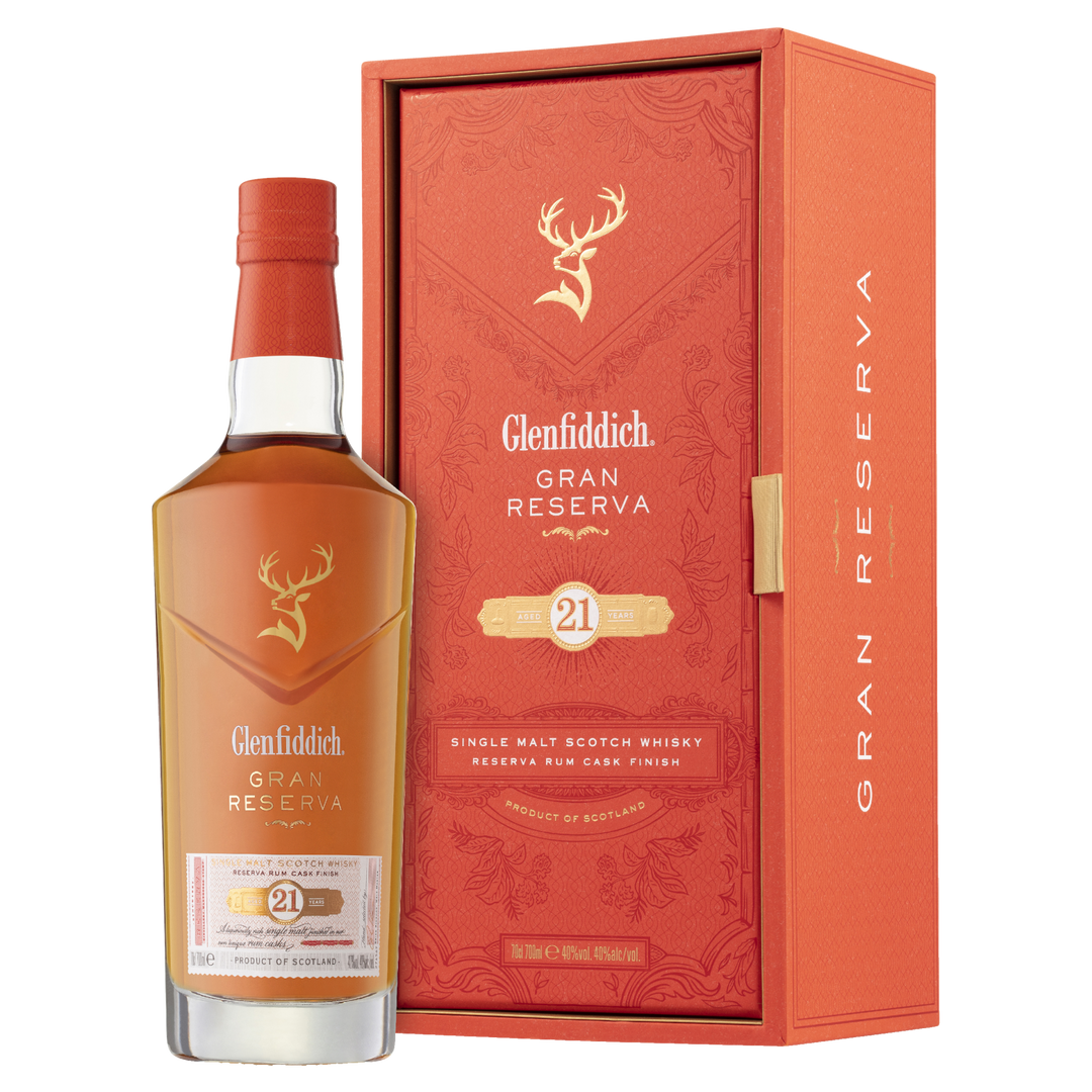 A bottle of Glenfiddich 21 Year Old Gran Reserva Single Malt Scotch Whisky, finished in Caribbean rum casks, stands beside its matching orange and gold box featuring the stag logo and refined detailing.