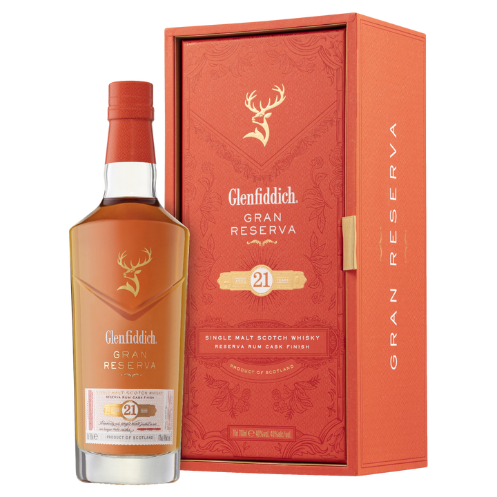 A bottle of Glenfiddich 21 Year Old Gran Reserva Single Malt Scotch Whisky, finished in Caribbean rum casks, stands beside its matching orange and gold box featuring the stag logo and refined detailing.