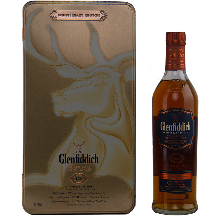 A Glenfiddich 125th Anniversary Edition Single Malt Scotch Whisky bottle stands beside a decorative gold tin adorned with an embossed stag and Glenfiddich branding, matured in European oak casks for added depth.
